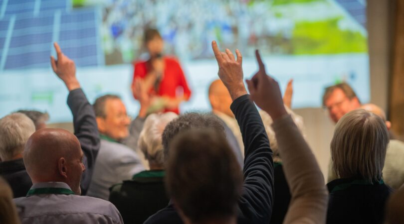 Groep mensen gefotografeerd van de achterkant die tijdens een bijeenkomst hun vingers opsteken voor vragen